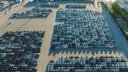 Overhead view of a parking lot filled with neatly arranged rows of new cars, casting long shadows in the light.
