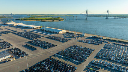 New cars parked in orderly rows at a port parking lot with the expansive Arthur Ravenel Jr. Bridge...