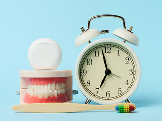 Plastic model of human jaw, alarm clock and dental floss on blue background - obrazy, fototapety, plakaty