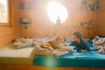 A teenage boy of 11 years old and his corgi dog woke up in a small house on a bed on a sunny morning