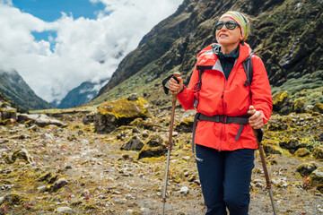 Portrait of Woman in sunglasses with backpack and trekking poles dressed red softshell jacket hiking on Makalu Barun National Park trek in Nepal. Mountain hiking, traveling and active people concept