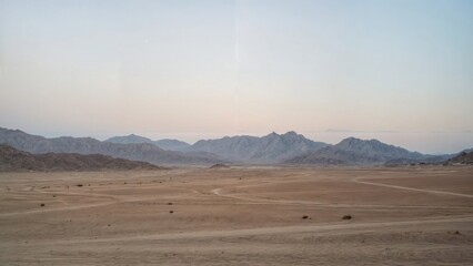 A desert landscape at dawn. Tracks in the sand against the background of the mountains.