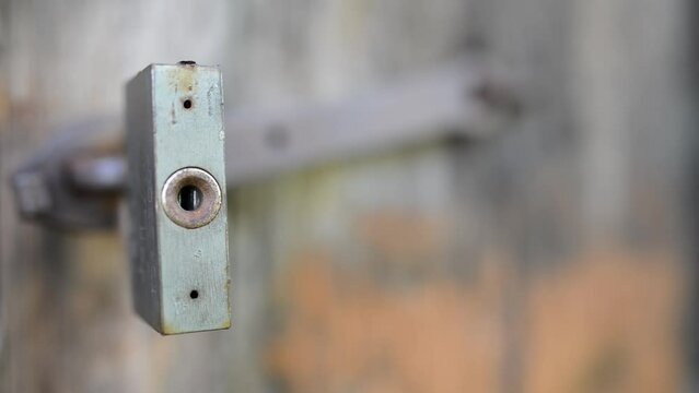Old metal lock swinging on a rusty hinge on a dilapidated wooden shed.
