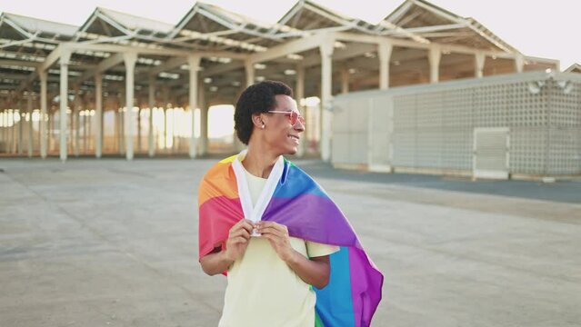 Cheerful African American non-binary person waving the LGBT rainbow flag celebrating gay pride day. Concept of LGBTQ diversity and inclusion.