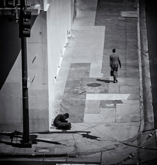 Above view of a man in a blue suit walking past a homeless person on a sidewalk in an urban setting