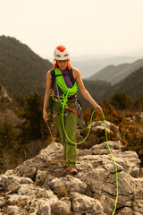 A woman is climbing a mountain with a green rope. She is wearing a green outfit and a red helmet
