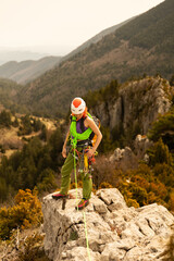 A woman is standing on a rock with a green rope around her waist. She is wearing a green jacket and a red helmet. Concept of adventure and excitement, as the woman is preparing to climb a mountain