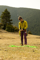 A man in a yellow shirt is standing in a field with a green rope. He is preparing to climb a mountain