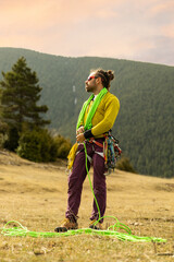A man in a yellow shirt and purple pants stands in a field with a green rope. He is looking up at the sky