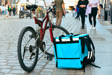 Delivery backpack stands on the road near a bicycle on a busy pedestrian street