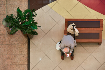 An elderly man sits on a bench with a smartphone, top view.