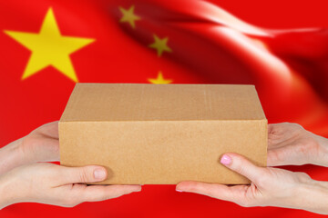 Parcel with Chinese flag. Cardboard box in hands. Trade exchange with China concept. Metaphor for ordering goods in PRC. Sending parcels from China. Delivery from people republic of China