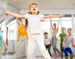 Group of positive juvenile boys and girls jumping cheerfully in dancehall during workout session