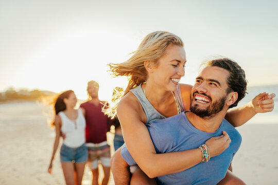 Group of friends running and laughing on the beach at sunset