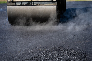 Closeup of a steamroller on freshly paved driveway to compact the hot asphalt, road construction...