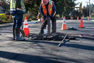 Construction workers using a jackhammer to dig up freshly laid asphalt to find the sewar access...