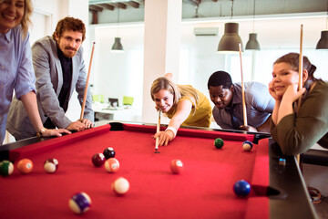 Diverse young people playing billiard in the office