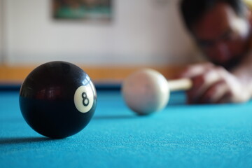 Man hitting the white ball towards the black number 8 ball and the hole on a blue cloth snooker...