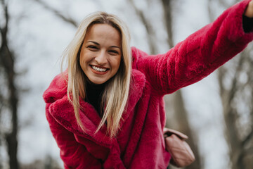 A cheerful, smiling woman wearing a vibrant pink fur coat is captured on a cold day, embodying...
