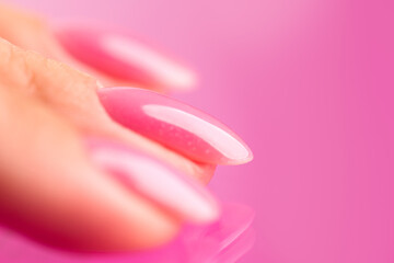 Pink nail polish on woman nails, shellac UV gel, varnish, manicure concept in beauty salon. Over pink background. Application of nail polish, healthy nails