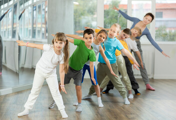 Obraz premium Group of focused tween children standing akimbo in row one by one, learning movements of folk dance in choreography lesson