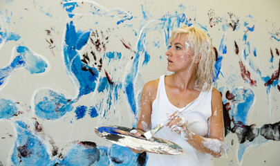 sexy beautiful pretty young artist woman female painter with blond hair in white casual underskirt paints with Brush an artwork on the studio wall