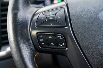 A steering wheel with a variety of buttons including a volume button and a call button. The buttons are black and the steering wheel is made of leather