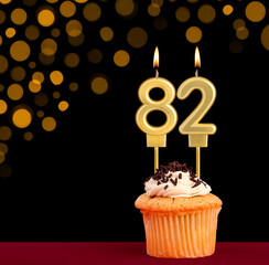 Number 82 birthday candle - Cupcake on black background with out of focus lights