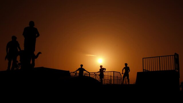 Children relax on skateboard ramp. Sporty children silhouette pass free time on the skateboard ramp during summer bright evening. A concept of active lifestyle during childhood.
