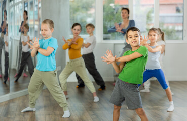 Dynamic little boy training hip hop dance poses with instructor and other attendees of dancing courses