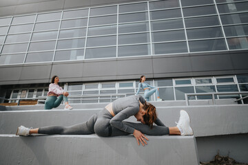 Three women in active wear practicing stretches on steps outside a modern building, focusing on...
