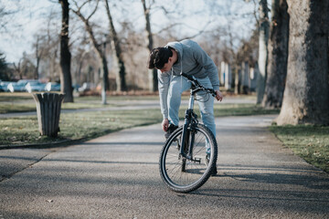Casual male cyclist pauses during a bike ride in an urban park with trees and pathway.