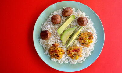 Spicy meatballs with corn fritters and sliced avocado on a bed of basmati rice.