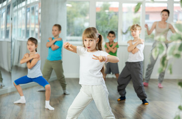 Dynamic little girl training break-dance poses in dancehall with trainer and other attendees of...