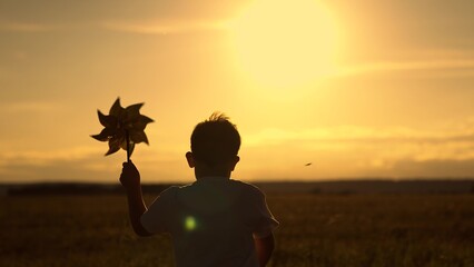 Child boy runs with toy wind pinwheel in his hand on summer field, sun day. Happy child playing...