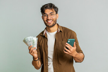 Indian man looking smartphone display sincerely rejoicing win, receiving money dollar cash...