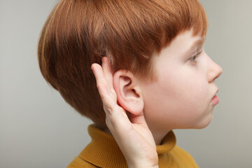 Little boy with hearing problem on grey background, closeup