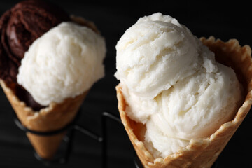 Ice cream scoops in wafer cones on stand against dark background, closeup