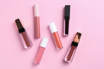 Different lip glosses on pink background, flat lay