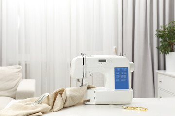 Sewing machine, measuring tape, scissors and fabric on white table in workshop