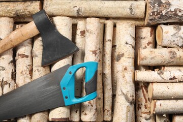 Saw with light blue handle and axe on firewood, flat lay