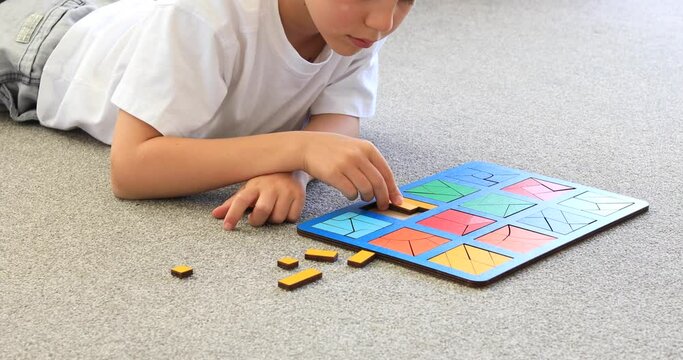 A boy is playing a logical wooden game on the carpet. Educational toys