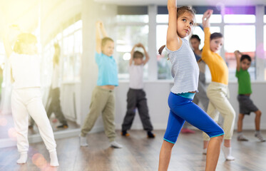 During dance workshop, girl with team of young like-minded children learn to dance modern dances, doing movement with unrecognizable teacher. Studio school for amateur and professional dancers