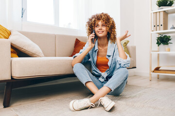Happy woman, holding mobile phone, enjoys online gaming while sitting on cozy sofa in the living room of her beautiful apartment.