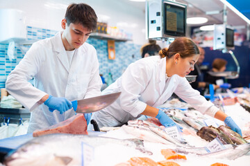 Confident seller with knife cut fish in supermarket near counter