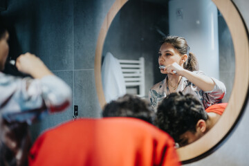 Mother multitasking in the bathroom, simultaneously getting ready and brushing her teeth while...