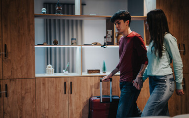 A young man and woman holding hands appear to be leaving their home, dragging a suitcase, ready for a journey. - obrazy, fototapety, plakaty
