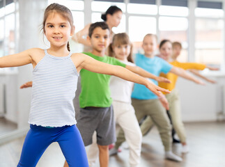 Positive juvenile girl engaged in choreography exercises together with children's group