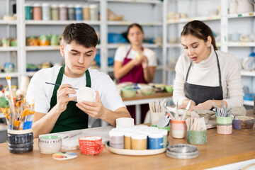 Fototapeta premium Young man and young woman making pottery from clay in workshop