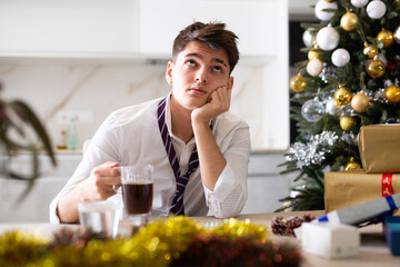 Young lonely man drinking alcohol at the christmas table at home